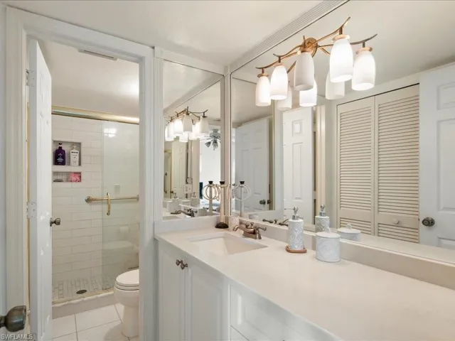 Renovated primary bath with new vanity, Corian counter, glass doors to shower, decor lights and mirror.