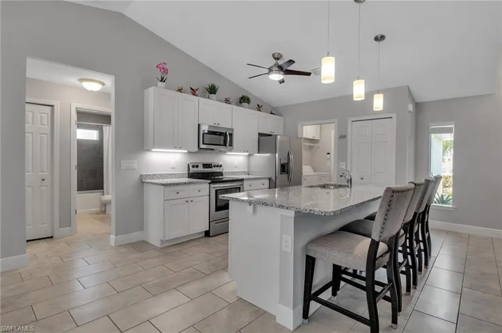 Kitchen featuring ceiling fan, stainless steel appliances, light tile flooring, decorative light fixtures, and white cabinets