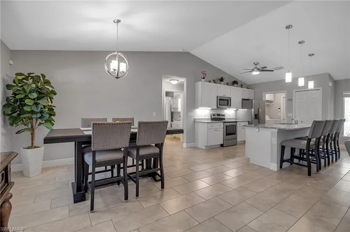 Dining space featuring high vaulted ceiling, sink, light tile floors, and ceiling fan with notable chandelier