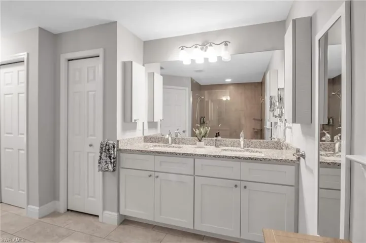 Bathroom with tiled shower, double sink vanity, and tile floors