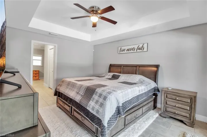 Tiled bedroom with connected bathroom, ceiling fan, and a raised ceiling