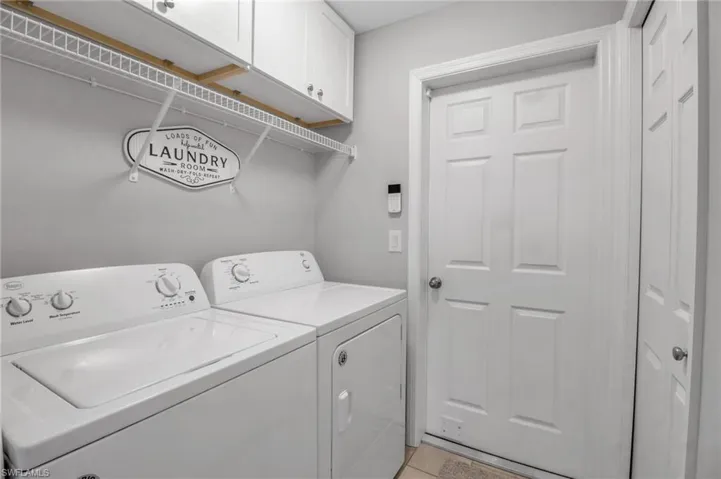 Laundry room featuring washer and clothes dryer, light tile flooring, and cabinets