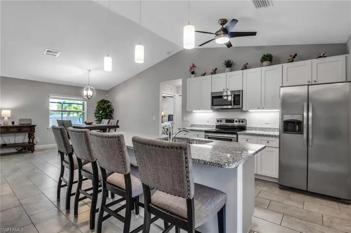 Kitchen featuring an island with sink, stainless steel appliances, lofted ceiling, and white cabinetry