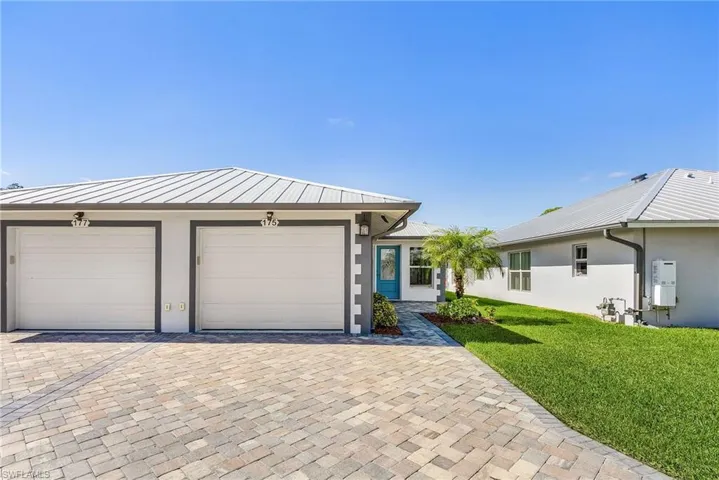 Single story home with stucco siding, a metal roof, a front lawn, a standing seam roof, and driveway