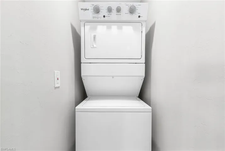 Laundry room featuring a textured wall and stacked washer / drying machine