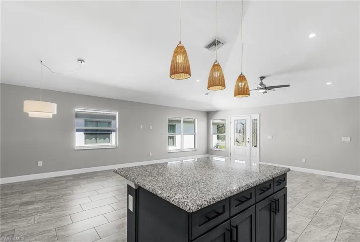Kitchen featuring dark cabinets, open floor plan, light stone countertops, hanging light fixtures, and a center island