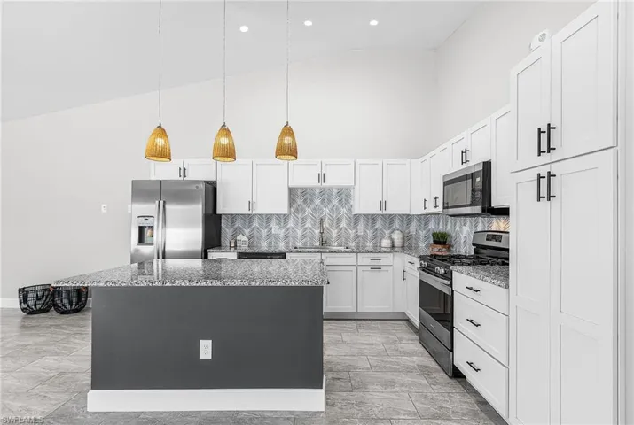 Kitchen with high vaulted ceiling, hanging light fixtures, a center island, appliances with stainless steel finishes, and white cabinetry
