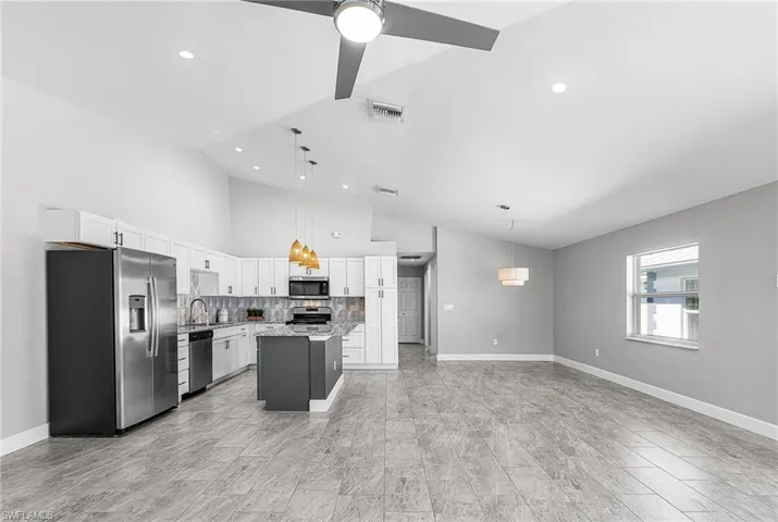 Kitchen featuring stainless steel appliances, a kitchen island, decorative backsplash, decorative light fixtures, and vaulted ceiling