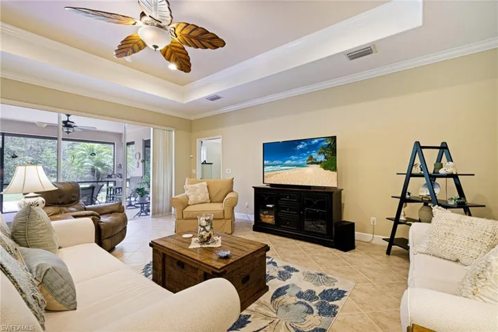Living area featuring a raised ceiling, light tile patterned flooring, ornamental molding, and a ceiling fan