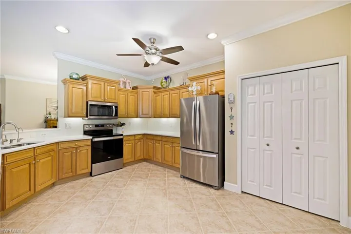 Kitchen with stainless steel appliances, ceiling fan, light countertops, ornamental molding, and light tile patterned floors