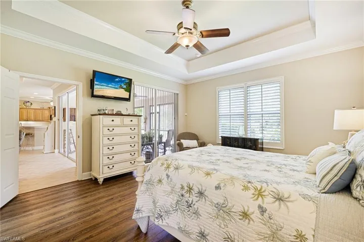 Bedroom featuring dark wood-style floors, ornamental molding, a tray ceiling, access to exterior, and a ceiling fan
