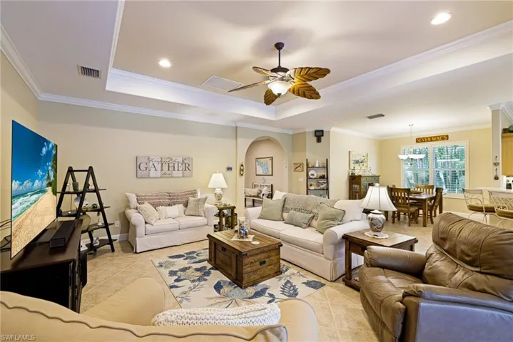 Living room with a raised ceiling, a ceiling fan, light tile patterned flooring, arched walkways, and recessed lighting