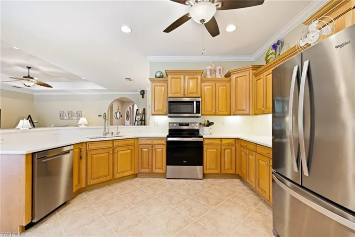 Kitchen featuring appliances with stainless steel finishes, ceiling fan, ornamental molding, a peninsula, and light countertops