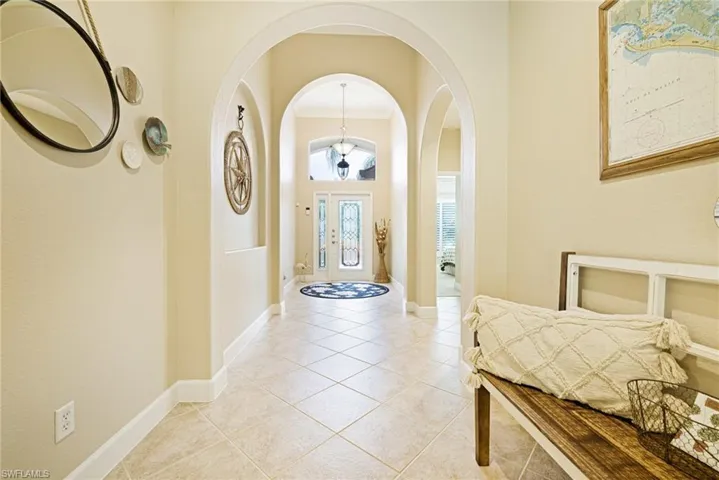 Foyer entrance with arched walkways, light tile patterned flooring, and crown molding