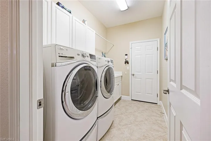 Laundry room with washer and clothes dryer, light tile patterned floors, and cabinet space