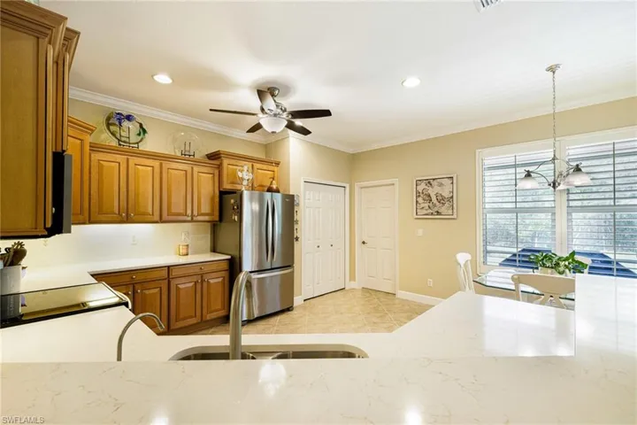 Kitchen with freestanding refrigerator, brown cabinetry, ceiling fan, hanging light fixtures, and crown molding