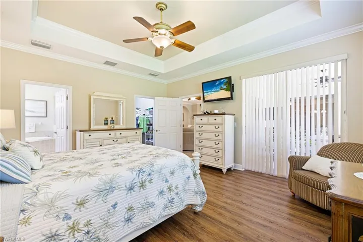 Bedroom with a raised ceiling, wood finished floors, crown molding, ensuite bath, and ceiling fan