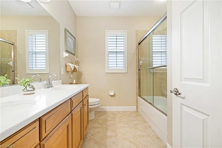 Bathroom featuring healthy amount of natural light, double vanity, tile patterned flooring, and combined bath / shower with glass door