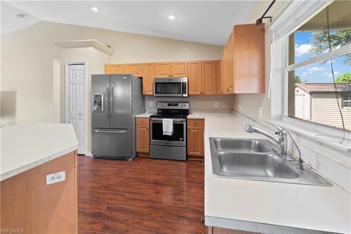 Kitchen with appliances with stainless steel finishes, vaulted ceiling, sink, and dark wood-type flooring