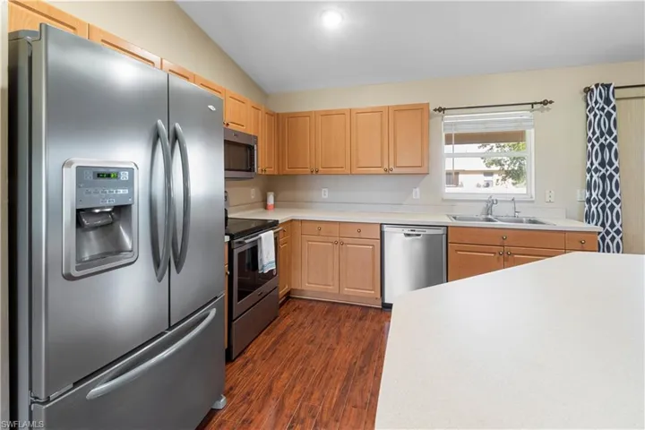 Kitchen featuring dark hardwood / wood-style floors, stainless steel appliances, sink, light brown cabinets, and lofted ceiling