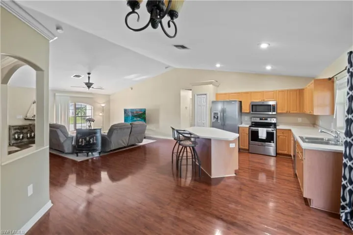 Kitchen featuring vaulted ceiling, a center island, ceiling fan, dark wood-type flooring, and appliances with stainless steel finishes