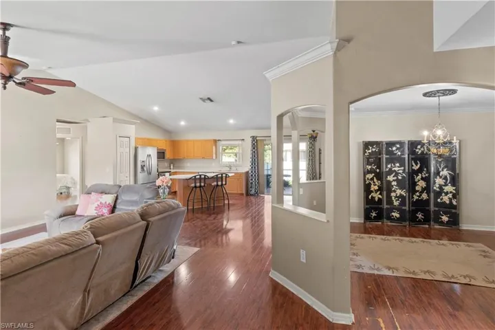 Living room with crown molding, ceiling fan with notable chandelier, high vaulted ceiling, and dark hardwood / wood-style flooring