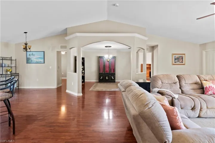 Living room with crown molding, dark hardwood / wood-style flooring, ceiling fan with notable chandelier, and lofted ceiling