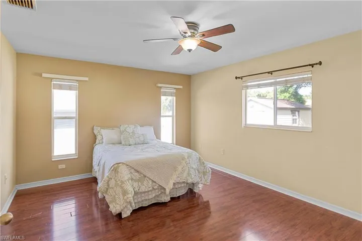 Bedroom with dark hardwood / wood-style flooring, ceiling fan, and multiple windows