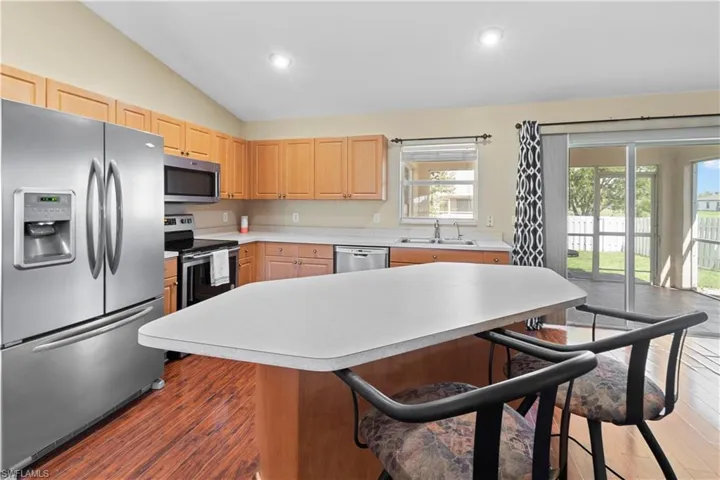 Kitchen with vaulted ceiling, dark hardwood / wood-style floors, appliances with stainless steel finishes, sink, and light brown cabinets