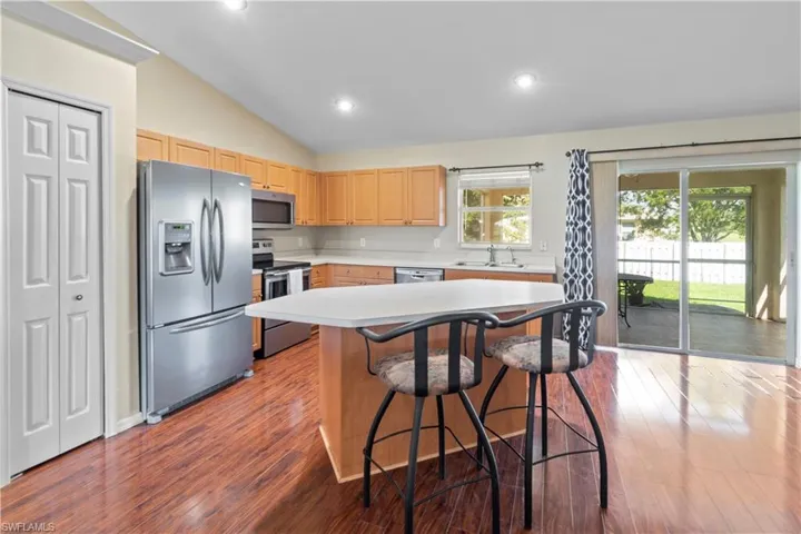 Kitchen with wood-type flooring, light brown cabinetry, sink, appliances with stainless steel finishes, and lofted ceiling