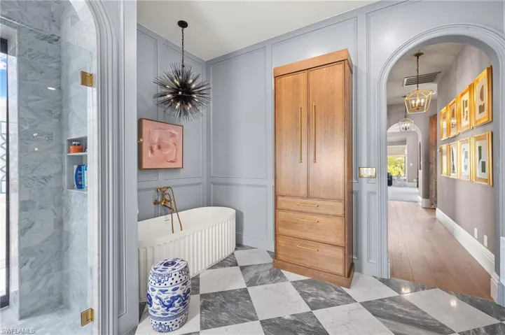 Full bathroom featuring a soaking tub, visible vents, a notable chandelier, and a decorative wall