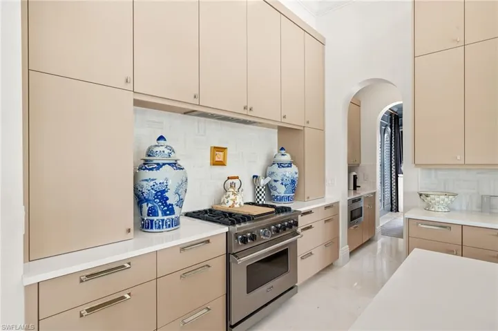 Kitchen with tasteful backsplash, arched walkways, stainless steel appliances, light countertops, and cream cabinetry