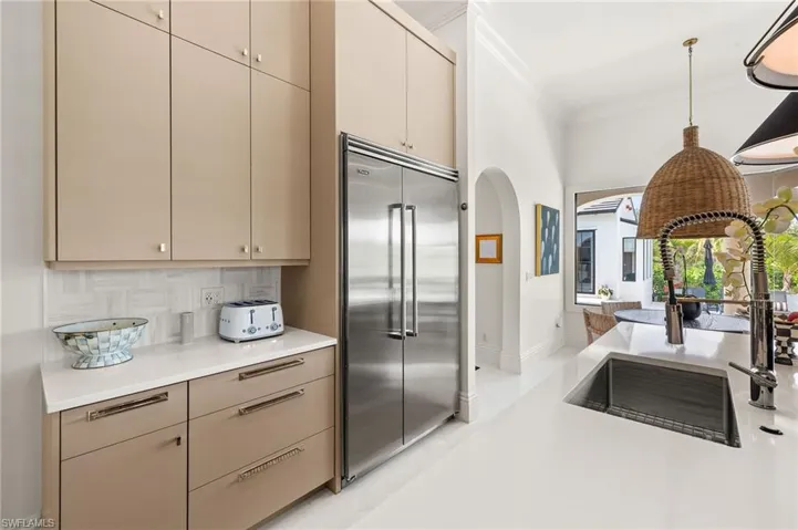 Kitchen with light countertops, ornamental molding, decorative light fixtures, stainless steel built in fridge, and backsplash