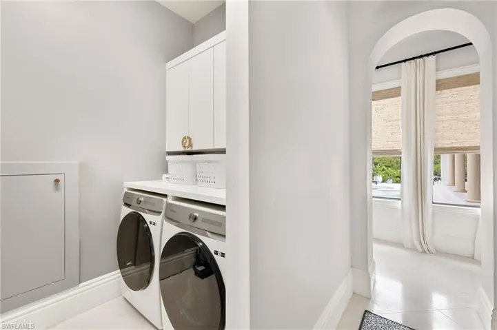 Laundry room with baseboards, cabinet space, light tile patterned flooring, and washing machine and clothes dryer