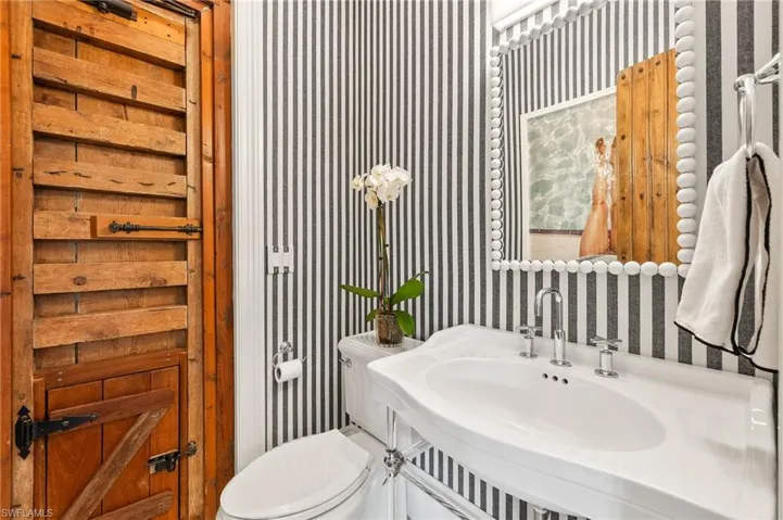 Half bath featuring wallpapered walls, toilet, and a sink