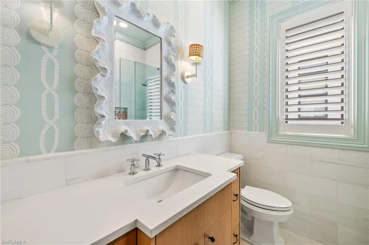 Full bath featuring a tile shower, wallpapered walls, a wainscoted wall, toilet, and vanity