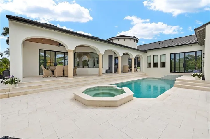 Rear view of property with stucco siding, a patio area, and a pool with connected hot tub