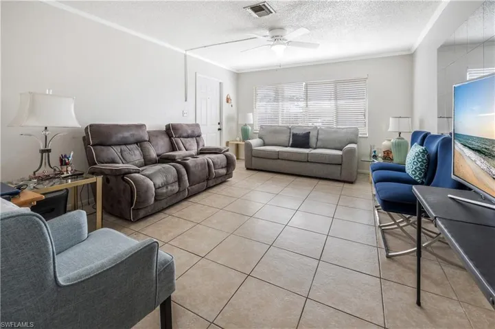 Living room featuring ceiling fan, crown molding, light tile patterned flooring, and a textured ceiling