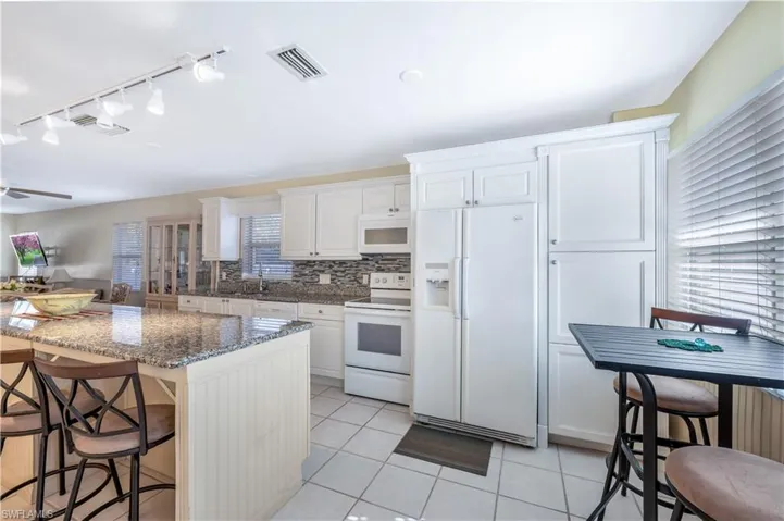 Kitchen featuring a kitchen bar, white appliances, light tile patterned floors, dark stone countertops, and white cabinetry