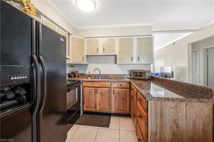 Kitchen featuring light tile patterned flooring, sink, ornamental molding, and black appliances