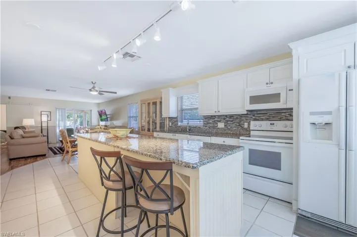 Kitchen featuring a kitchen breakfast bar, a center island, white appliances, and white cabinetry