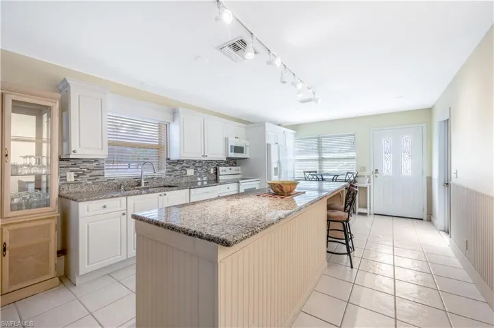 Kitchen featuring a center island, white cabinets, white appliances, and sink