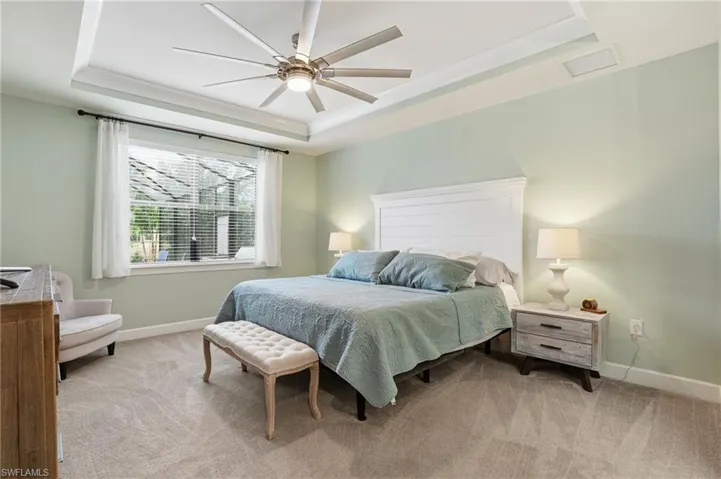 Bedroom with a tray ceiling, light colored carpet, and a ceiling fan