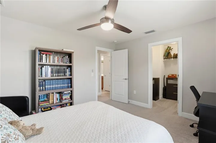 Bedroom with a spacious closet, light carpet, a desk, and ceiling fan