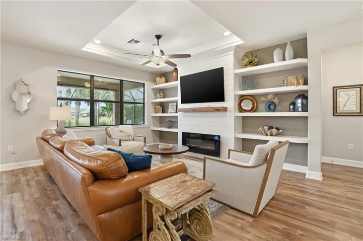 Living room with a large fireplace, light wood-type flooring, a ceiling fan, a raised ceiling, and recessed lighting