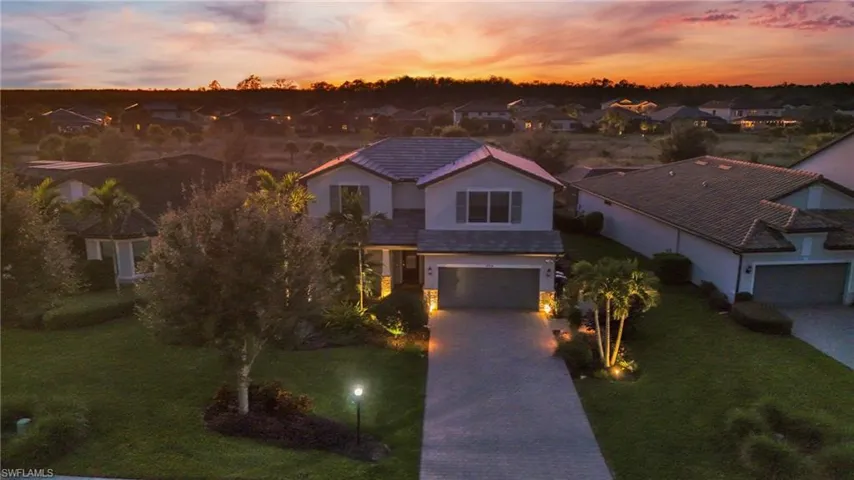 View of front of property with decorative driveway, a lawn, stone siding, and a tiled roof