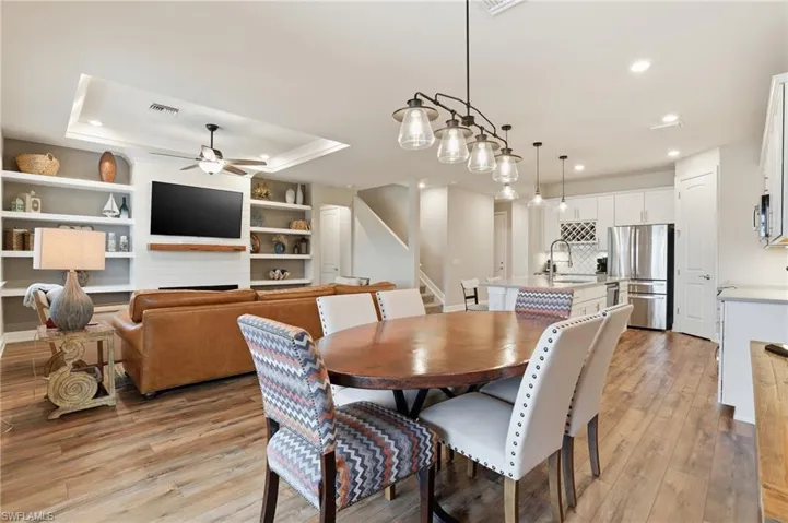 Dining area featuring a ceiling fan, stairs, light wood-type flooring, a large fireplace, and a raised ceiling
