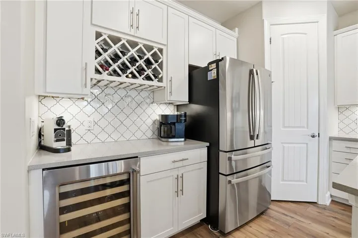 Kitchen with decorative backsplash, white cabinetry, wine cooler, and light wood-style floors