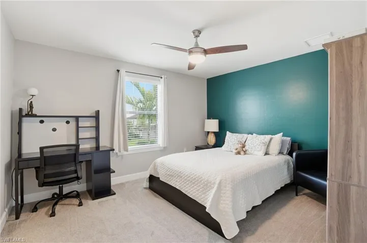 Bedroom with light colored carpet, ceiling fan, and a desk
