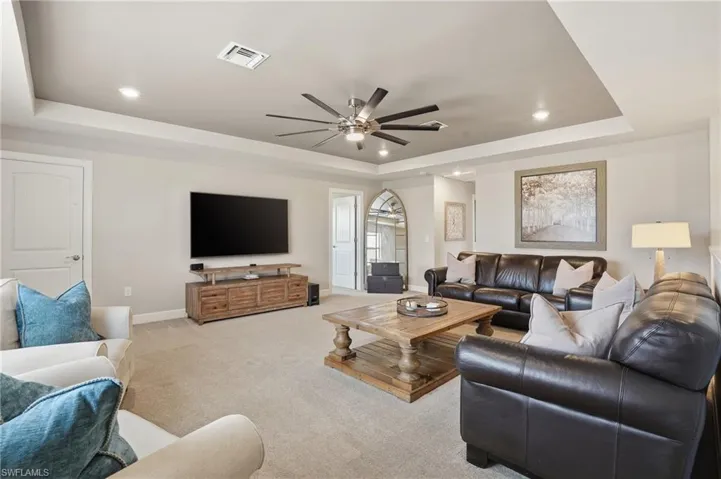 Living area with a tray ceiling, light colored carpet, recessed lighting, and ceiling fan